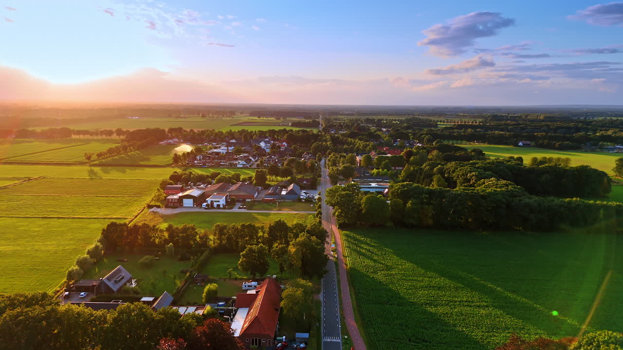 Sunset over green fields. A beautiful sunset casts warm light over a peaceful village surrounded by lush green fields and distant hills