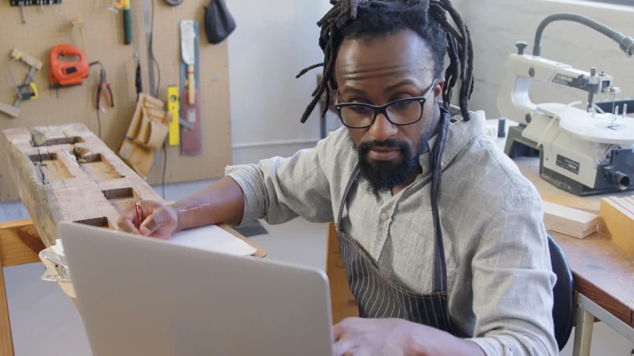 Carpenter writing in notepad while using computer 4k
