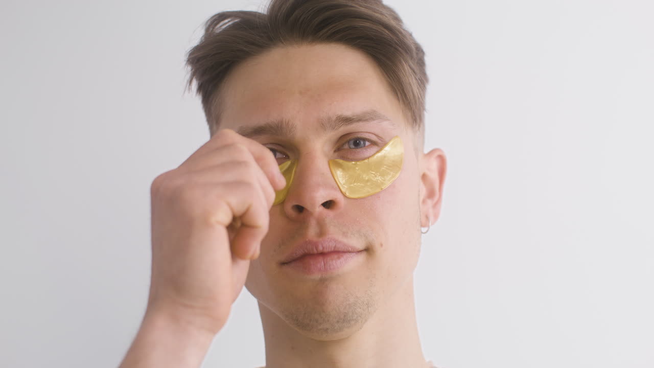 ung man använder och tar bort guldplåster för påsar under ögonen