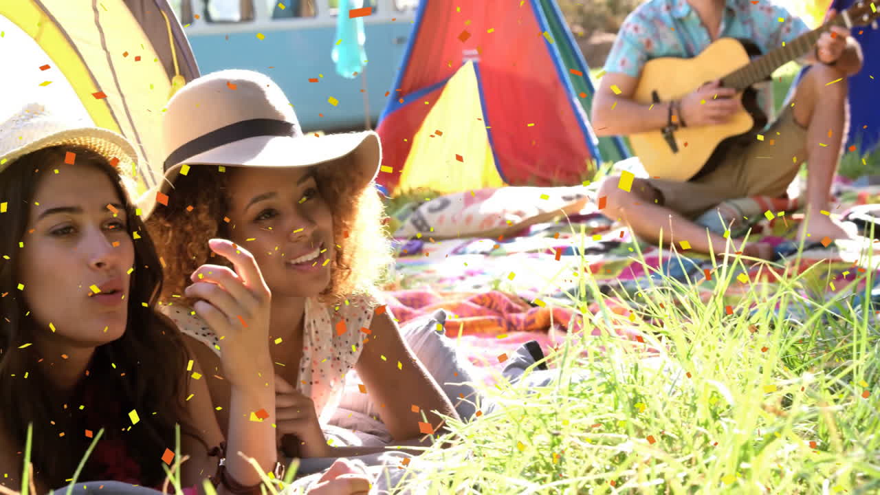 Confetti falling, people relaxing on grass with colorful tents in background