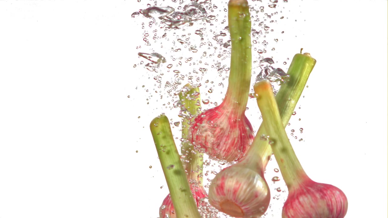 Bulbi d'aglio giovani freschi sommersi nell'acqua con bolle che salgono