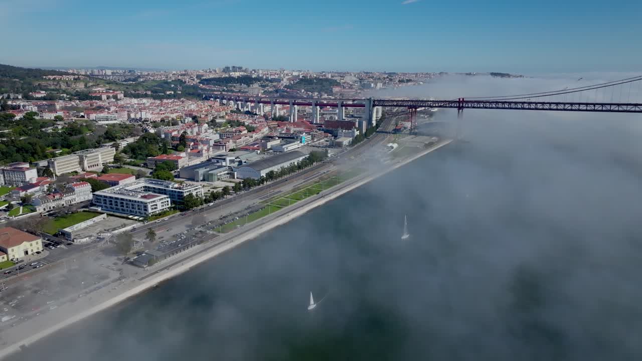 Drone shot of clouds, sailboats and the bridge in Lisbon.