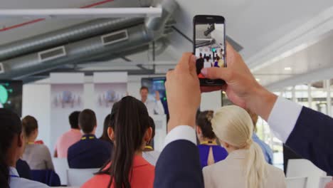 man in audience at a business conference filming with smartphone