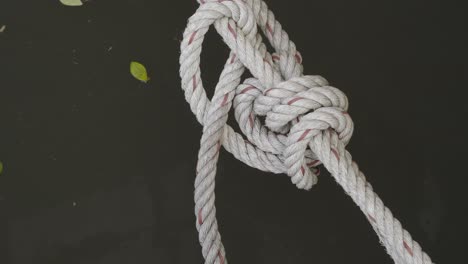 A-close-up-shot-of-a-knot-and-rope-securing-a-houseboat-to-the-bank-of-the-Khwae-Noi-river-in-Kanchanaburi,-Thailand