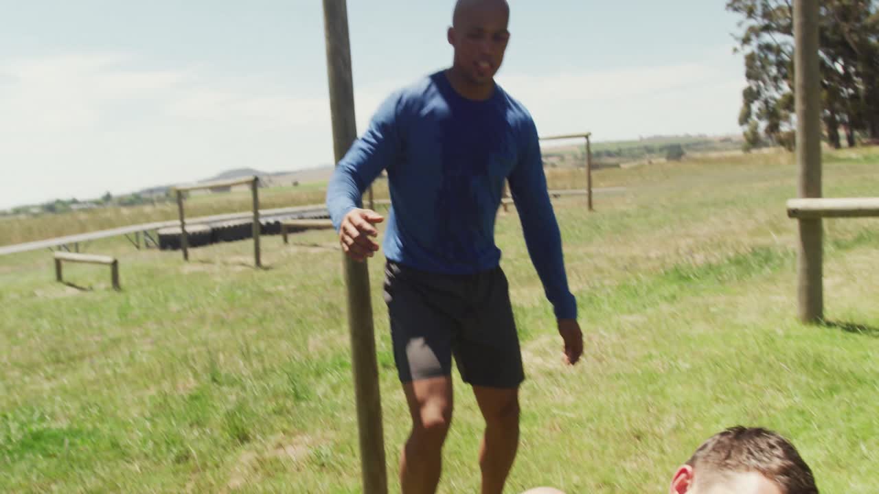 hombre caucásico en forma cayendo de las barras en una carrera de obstáculos ayudado por un colega afroamericano