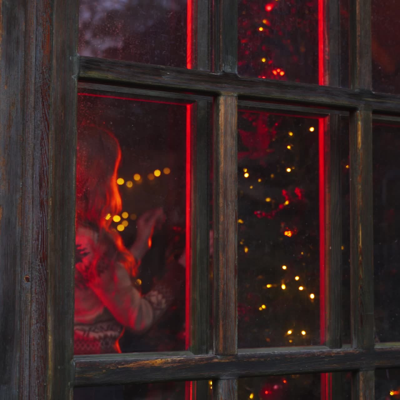 New year preparation. View from outdoors through the window on a woman decorating Christmas tree in the evening. New Year holidays.