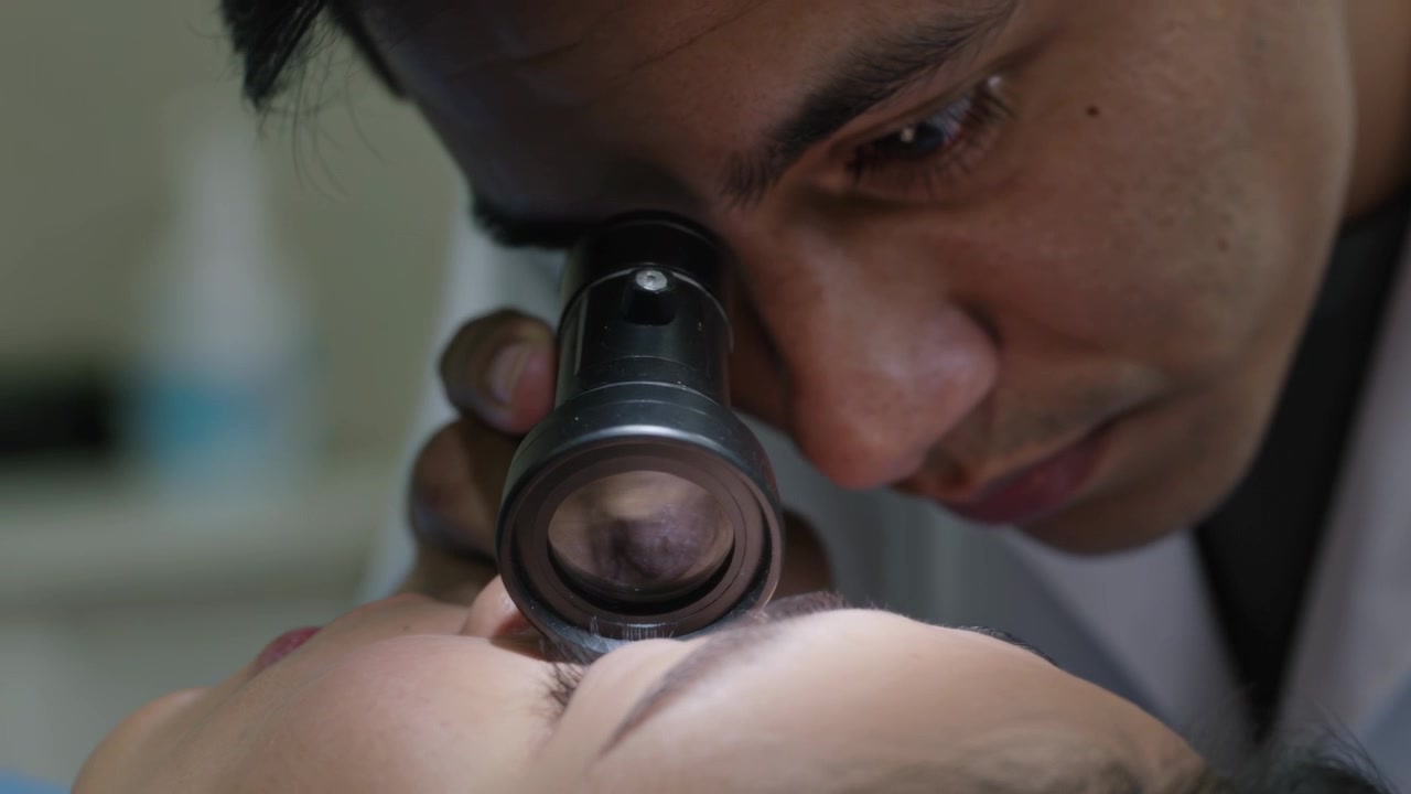 Avvicinando una lente d'ingrandimento, il medico si china e ispeziona la palpebra del paziente in clinica, indossando un camice da laboratorio.