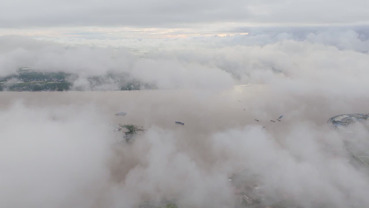 Aerial video of Phnom Penh with sweeping clouds partially obscuring the Tonle Sap river, as boats travel below and the skyline fades in and out of the mist