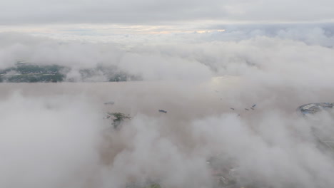 aerial video of phnom penh with sweeping clouds partially obscuring the tonle sap river, as boats travel below and the skyline fades in and out of the mist