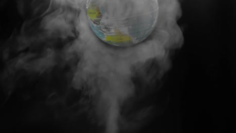 the simulated earth spins above steam smoke that shot up on a black background. concept of earth destroyed by pollution.