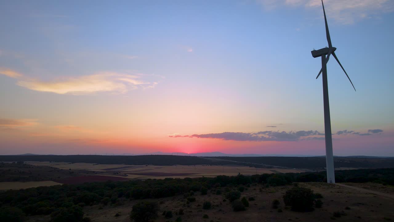 카메라는 낮은 태양을 배경으로 숲에서 풍력 터빈 농장 실루엣을 보여주기 위해 뒤로 물러납니다.