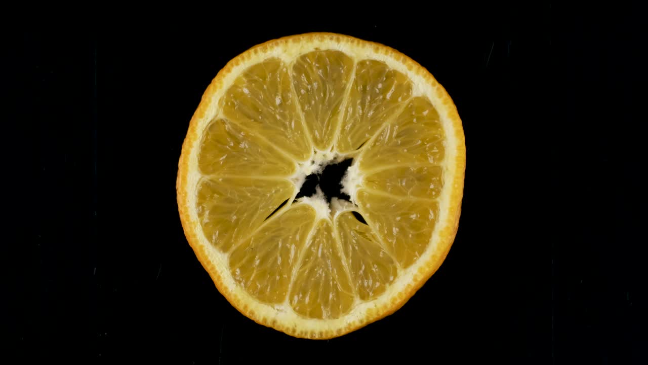 Rotation einer Mandarinenscheibe auf schwarzem Hintergrund