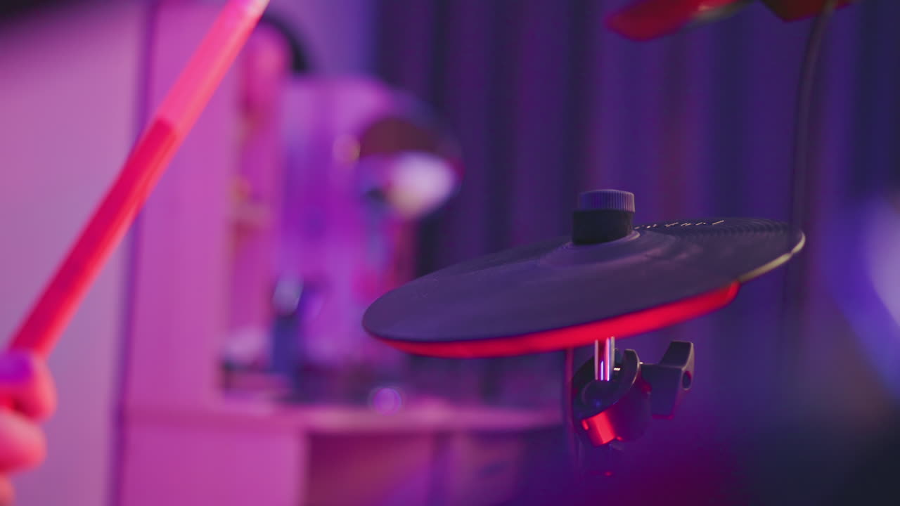 Close up electronic cymbal pad being struck by drummer with red drumstick illuminated by purple studio lights capturing motion blur and textured surface conveying rhythm