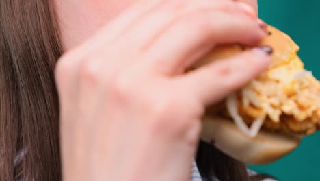 primer plano de una hembra mordiendo una hamburguesa en una pantalla verde. el concepto de nutrición y dieta no saludables