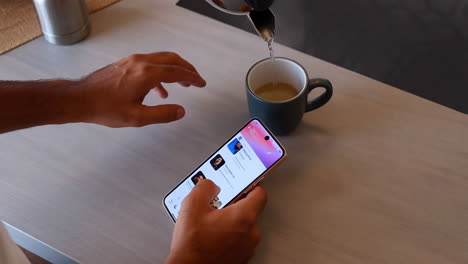 person pouring water into a mug while using a smartphone