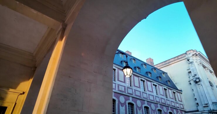 Ripresa in movimento attraverso la Reggia di Versailles che rivela archi monumentali in pietra, alte finestre, mascheroni scolpiti e dettagli architettonici storici francesi