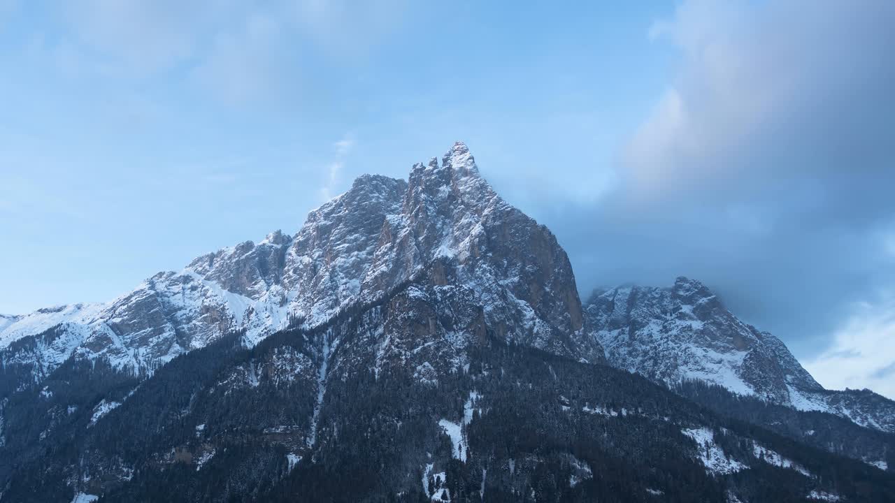 Drone video showcasing breathtaking, snow-capped peaks of the Italian Alps at sunrise, with warm sunlight illuminating rugged terrain under a sky dotted with soft clouds. Stunning aerial footage