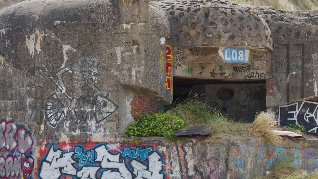 Static wide shot of abandoned concrete bunker with colorful graffiti, natural daylight, no visible movement