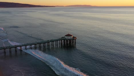 olas y muelle de la playa de manhattan al atardecer en california - estática aérea