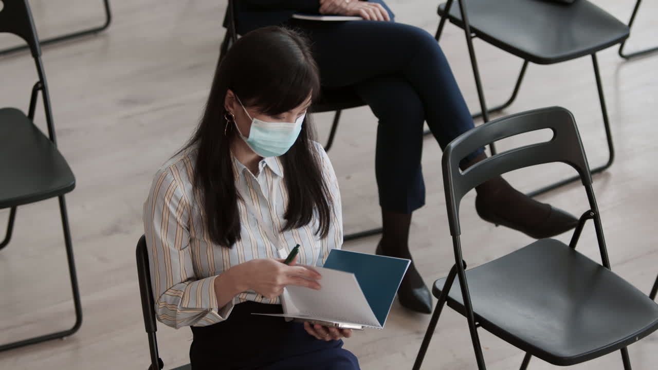 Businesswoman in Mask Leafing through Notebook
