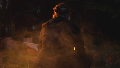 Young-person-sitting-outside-with-campfire