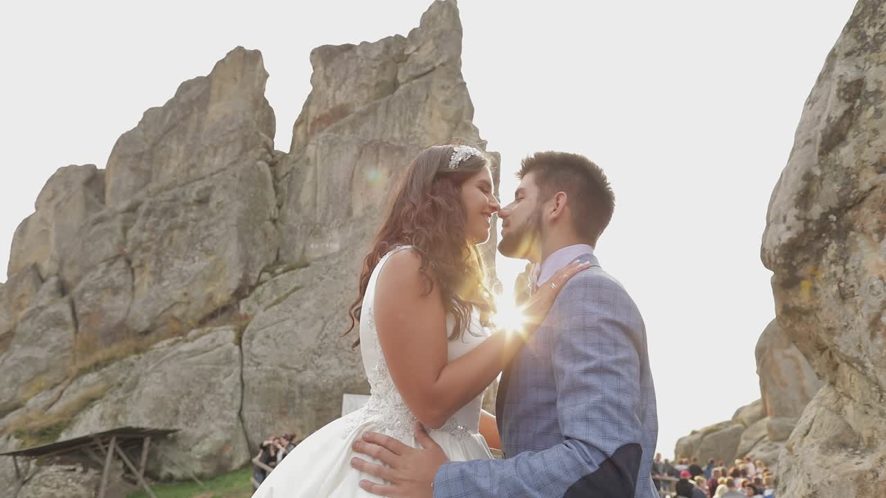 Sposo con la sposa vicino alle colline montuose. Coppia di sposi innamorati. Raggi di sole.