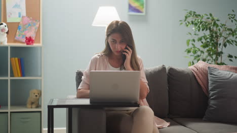 woman with laptop talks via phone near daughter on sofa