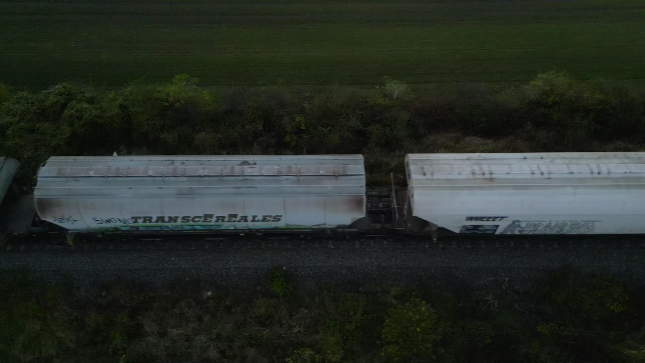 Freight train with weathered cars moving through rural landscape at dusk, aerial view