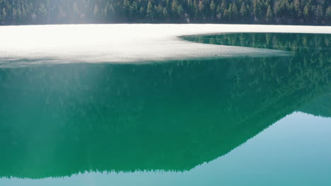 aerial orbit of mountain reflection in a semi frozen lake