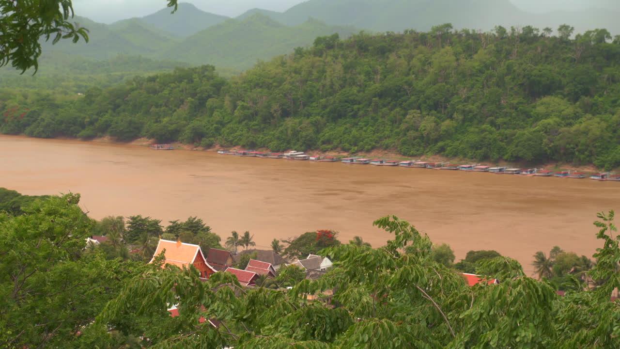 Fiume Mekong fangoso con barche e case sul fiume nella foresta a Luang Prabang, Laos, durante un temporale