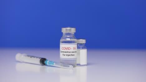 botellas de vacuna contra el coronavirus en la mesa de laboratorio de fondo. jeringa cerca para covid-19. concepto de derrotar el coronavirus. pantalla azul, llave de croma. cerca. cámara lenta