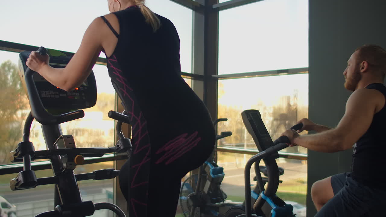 피트니스 의 카디오 구역에서 한 무리의 사람들이 여성의 타원형 운동 자전거를 사용합니다.