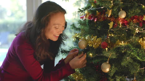 Glückliche-Biracial-Frau-Schmückt-Weihnachtsbaum-Und-Lächelt,-Zeitlupe