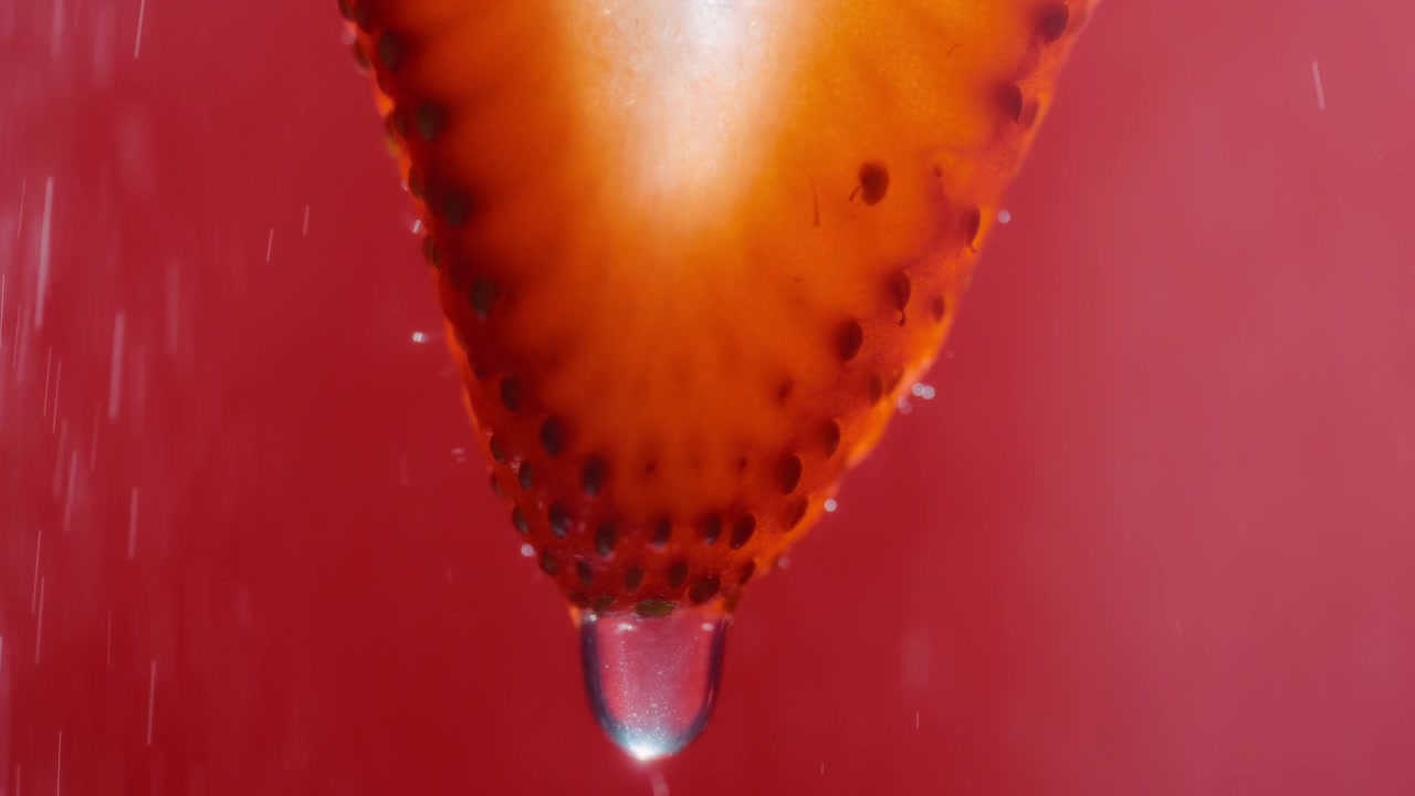 Goccia d'acqua che cade da una fetta di fragola con schizzi d'acqua sullo sfondo.