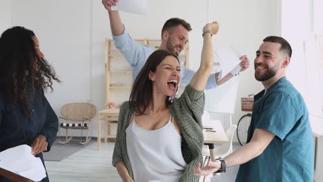 overjoyed carefree multiracial team throw papers dance together in office