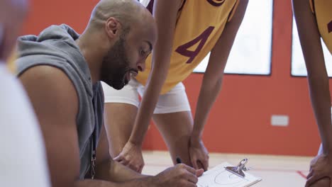 happy diverse female basketball team training with male coach in indoor court, in slow motion