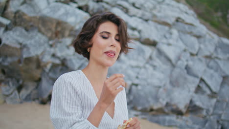 mujer al aire libre comiendo bocadillos en la orilla del mar de cerca. hermosa chica tímida descansando