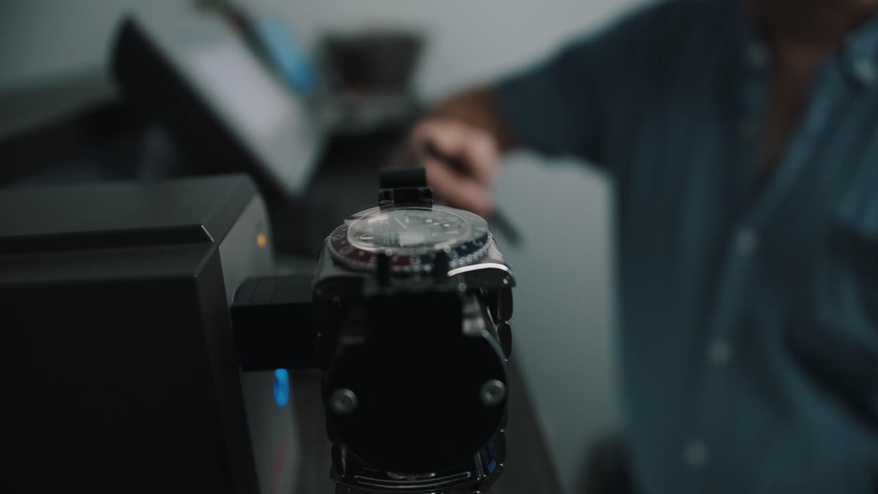 A watchmaker waiting in the background for the timegrapher to compete it's reading for the watch - close up