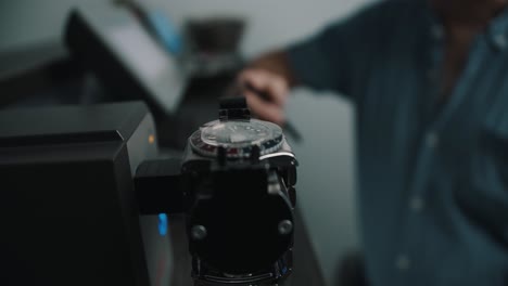 a watchmaker waiting in the background for the timegrapher to compete it's reading for the watch - close up