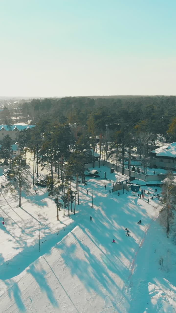 snowy mountain with modern ski resort and comfortable track among pine forest against endless blue sky aerial view