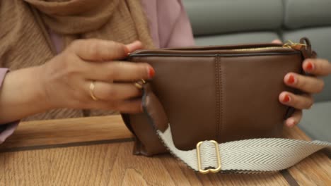 woman opens her brown leather handbag