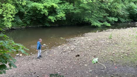 young boy throwing stones into a woodland river and having fun