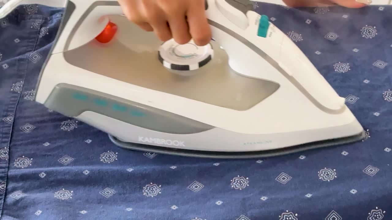 A close-up view of a steam iron removing wrinkles from a blue patterned shirt