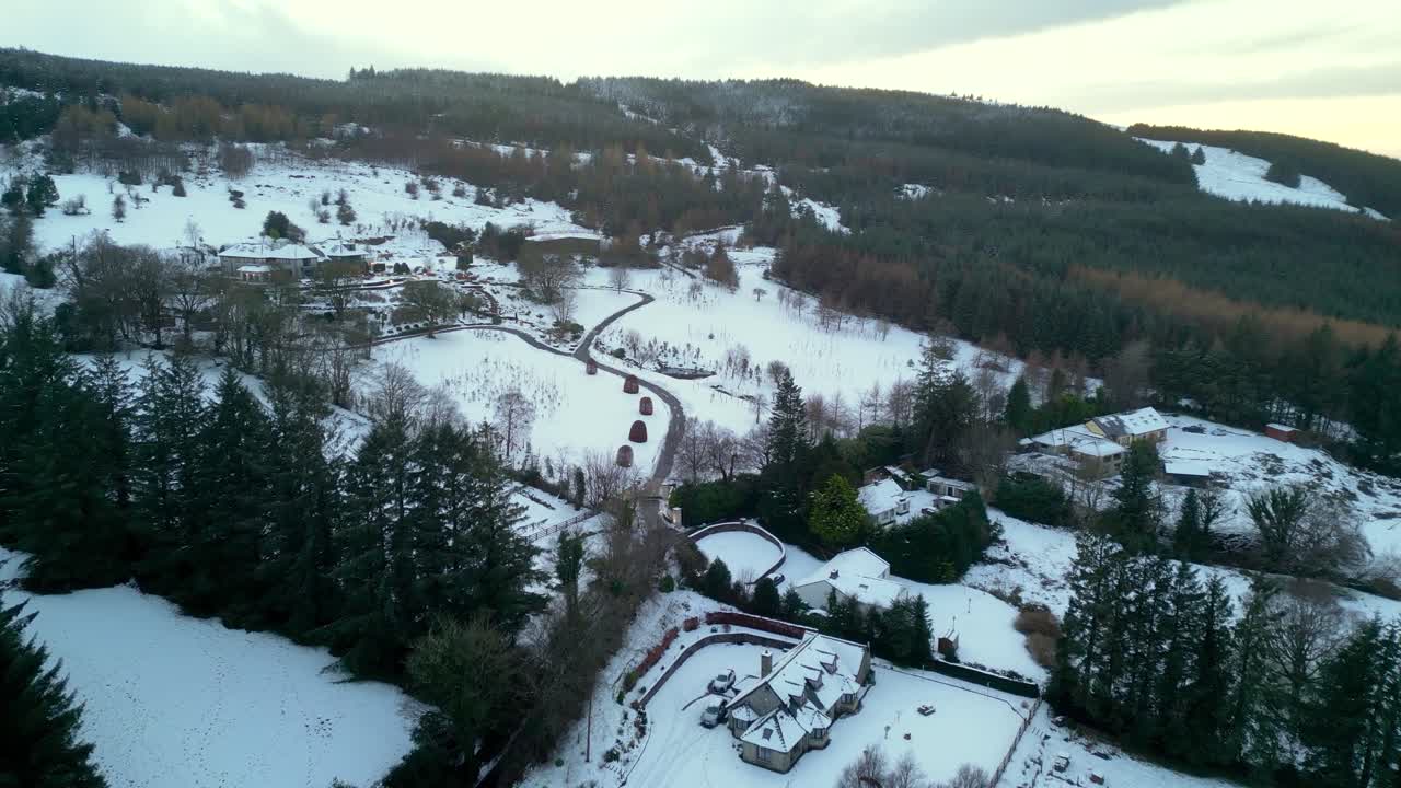 Aerial view of snow-covered Dublin Mountains in winter. Rural houses, winding roads, and forested hills under a soft, cloudy sky. Peaceful Irish countryside landscape.