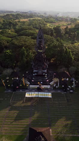 vertical aerial view of a sacred hindu temple in bali on a sunny day, displaying traditional balinese architecture, elaborate stonework, and peaceful surroundings of green vegetation