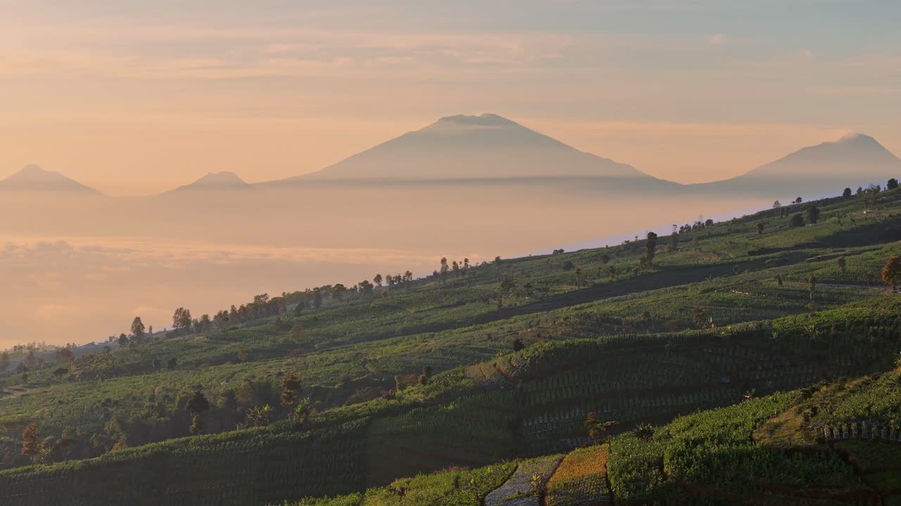 Drone footage capturing majestic mountain silhouettes rising above misty valleys during early morning light with Verdant agricultural hills in the foreground enhance the tranquil atmosphere