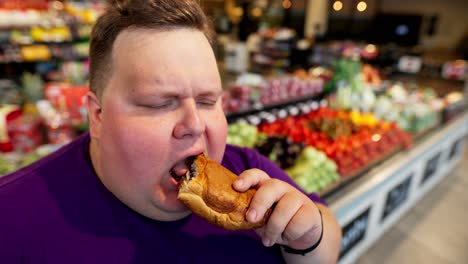 close-up shot of a happy overweight man with short hair wearing a purple t-shirt eating a croissant with chocolate filling in a supermarket