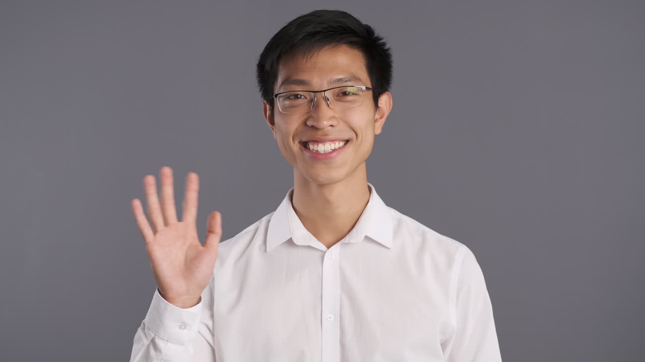 아시아인 남자가 미소 짓고 카메라를 향해 손을 흔들고 있습니다.