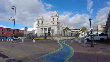 A-charming-city-street-adorned-with-a-majestic-white-cathedral,-set-against-a-backdrop-of-an-awe-inspiring-azure-sky