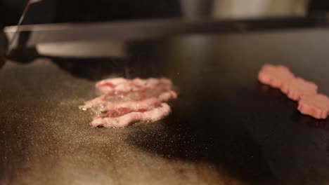 bacon strips frying, turning crispy on hot surface.